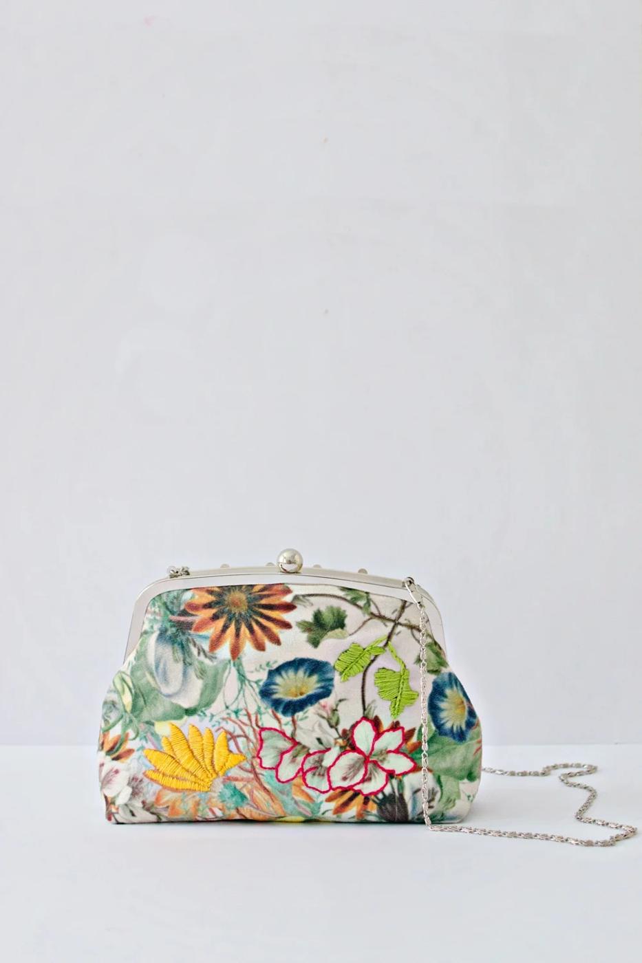 A small fabric purse with a silver metal clip frame, snapped shut and resting on a cream linen cloth.