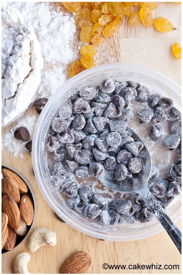 Bowl of chocolate chips dusted with flour and stirred with a spoon beside golden raisins, almonds and cashews