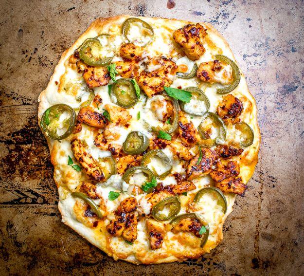 Rustic sheet pizza with spicy chicken pieces, melted white cheese and scattered pickled jalapeno slices