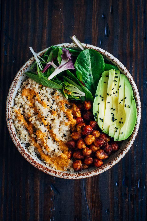 Vegan buddha bowl with quinoa, crispy spiced chickpeas, sliced avocado and mixed greens on a dark wood table