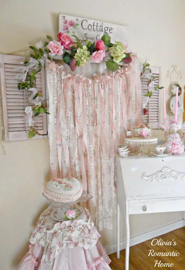 Pale pink and cream rag garland of torn fabric and lace strips hanging above a white dresser with flowers