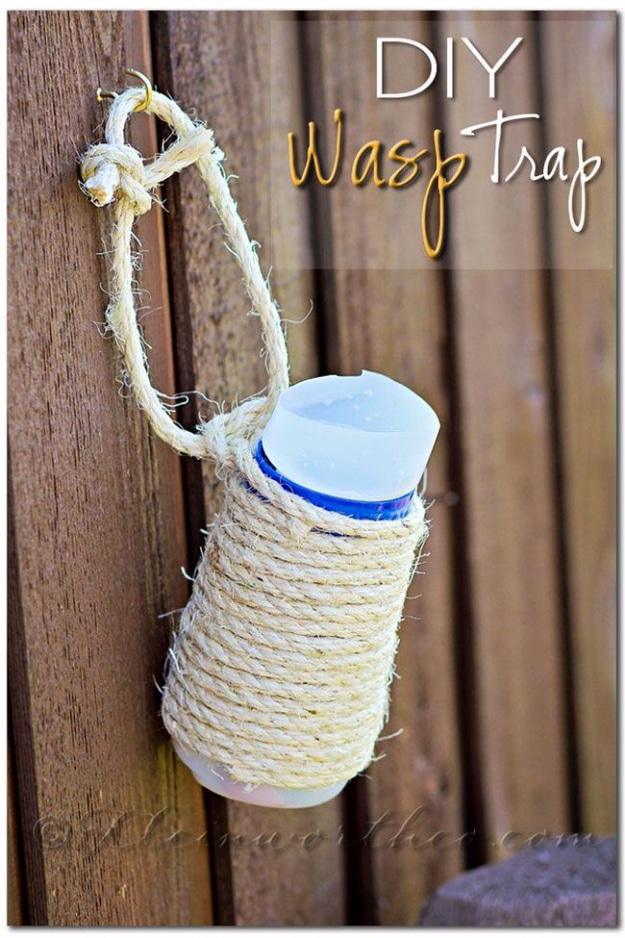 DIY wasp trap, a plastic bottle wrapped in cream colored twine hanging from a rope against a weathered wood fence