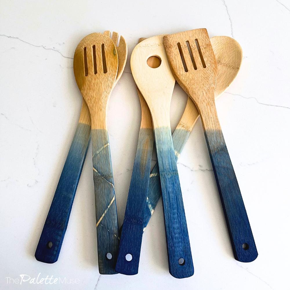 Five bamboo kitchen spoons with deep blue ombre dipped handles fanned out across a white marble counter