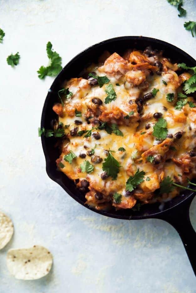 Butternut squash and black bean enchilada skillet in a cast iron pan topped with melted cheese and cilantro
