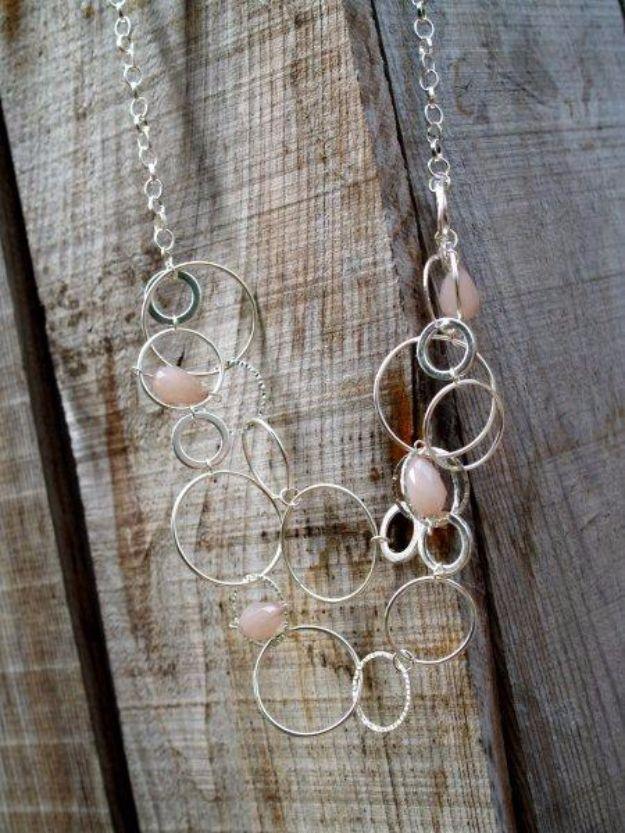 Anthropologie inspired shepherd moon necklace, two rows of linked silver rings with small pink beads on weathered wood