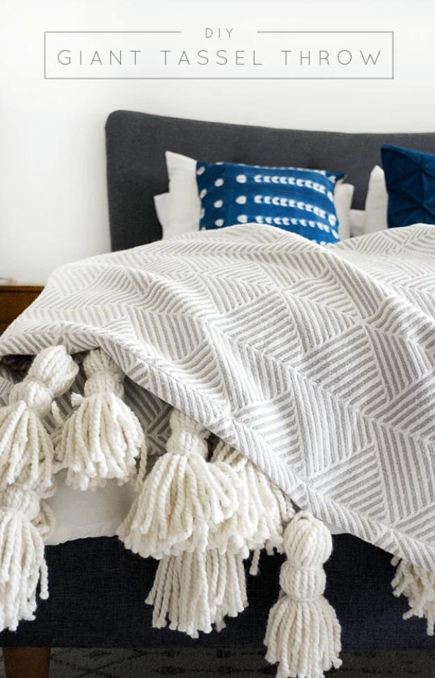 Gray and white patterned throw edged with five oversized cream yarn tassels across a bed, typeset title above