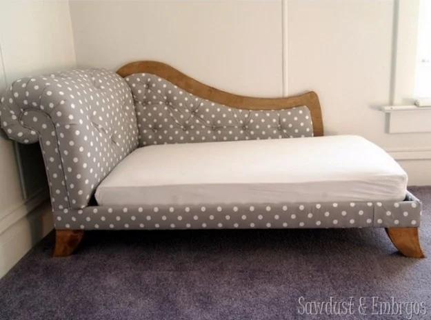 Gray and white polka dot fainting couch with a scrolled wooden crest along the back, against a pale wall