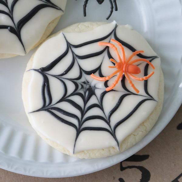 Round sugar cookie with white frosting, a black piped web and a small spider decoration on top for Halloween