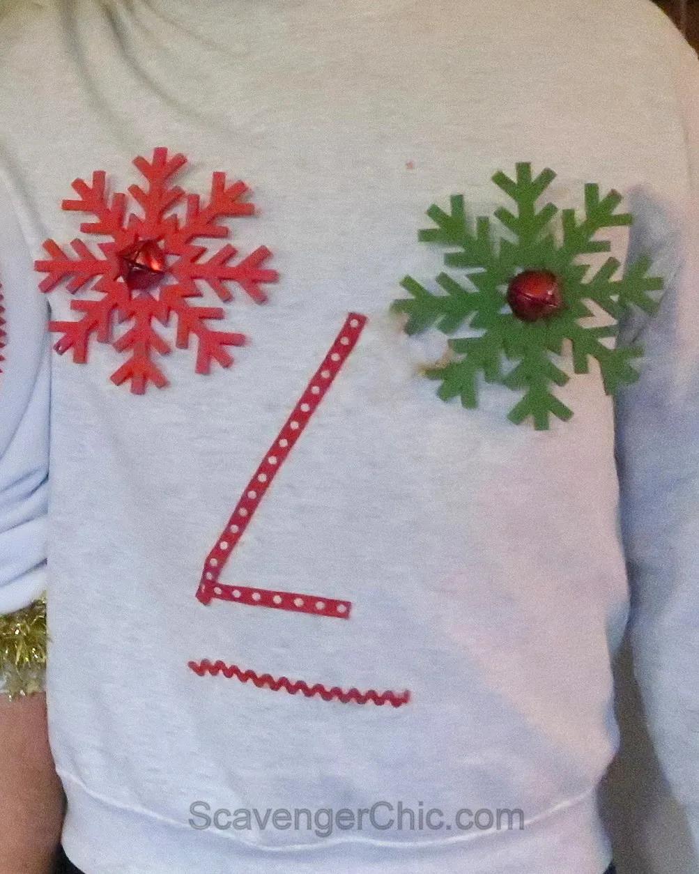 A white sweatshirt decorated with red and green glitter snowflakes with jingle bells, red polka dot ribbon and rickrack
