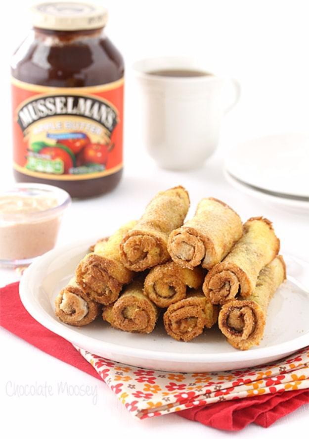 Apple butter french toast roll ups rolled in cinnamon sugar on a white plate beside a jar of apple butter