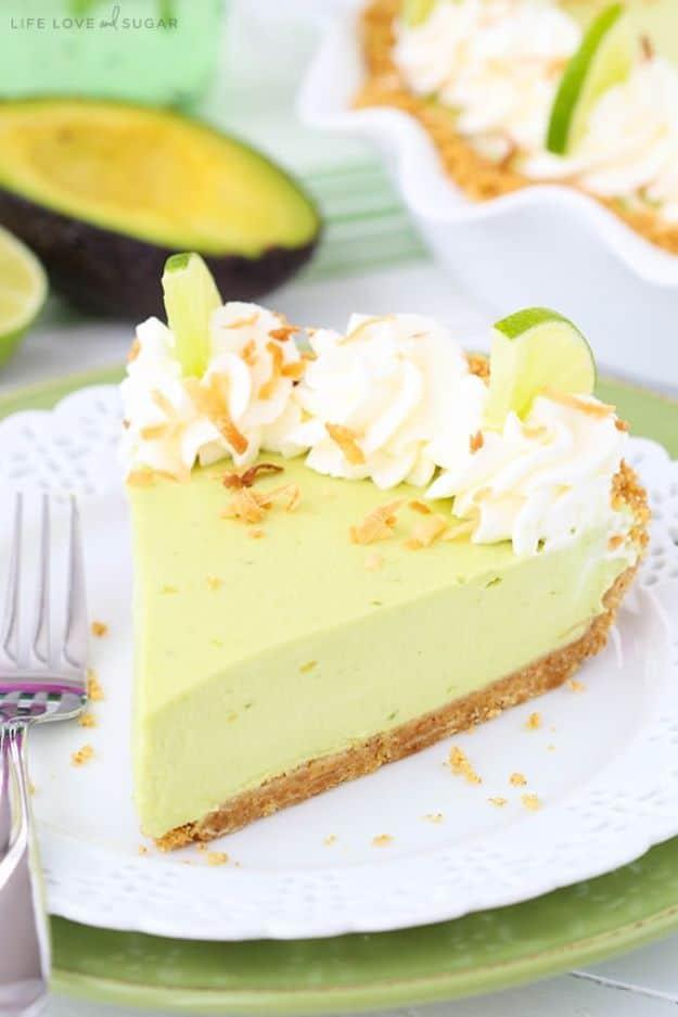 Pale green avocado key lime pie slice on a graham crust, whipped cream rosettes each holding a twisted lime slice