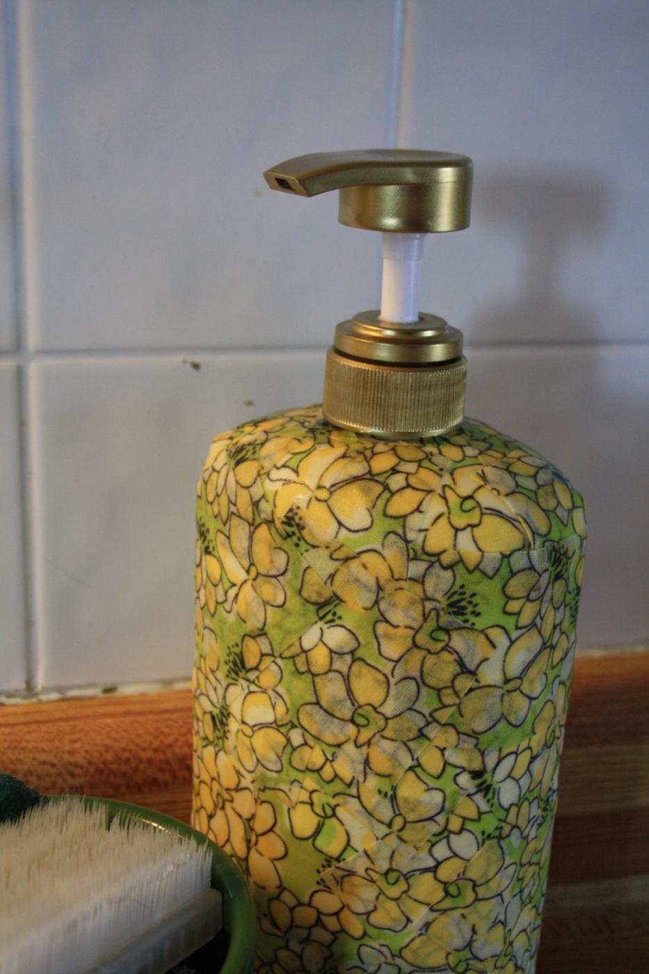 Large pump bottle covered in yellow and green floral fabric with a gold painted pump head beside a kitchen sink