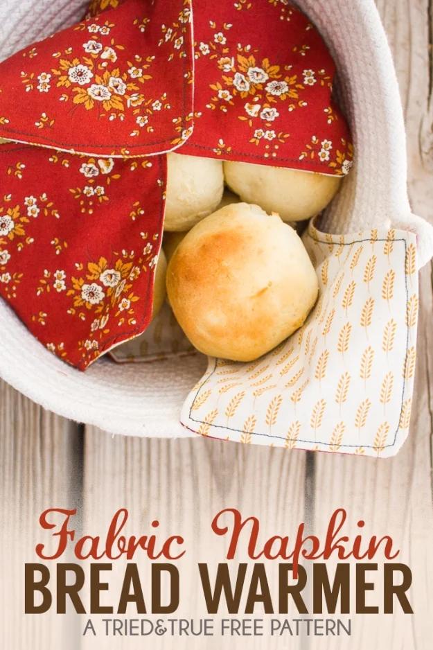 Red floral bread warmer folded over dinner rolls in a white basket, with a wheat print lining showing underneath