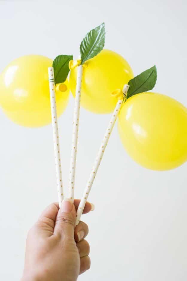 DIY baby shower decoration lemon balloons, three small yellow balloons with green leaves on patterned paper straws