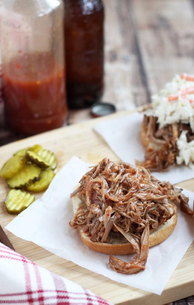 Vinegar sauced pulled pork on a board with pickles, an easy 3 ingredient slow cooker pork dinner recipe