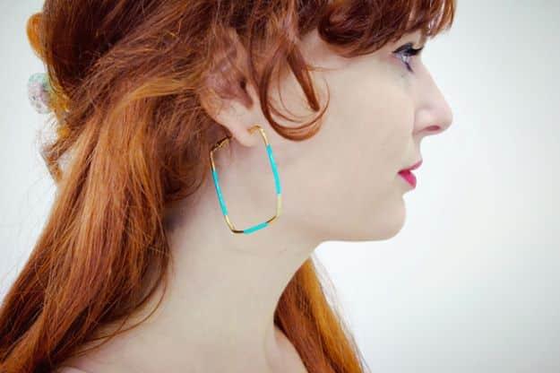 Square hoop earrings worn by a woman in profile with red hair, a gold hoop bent square and painted turquoise