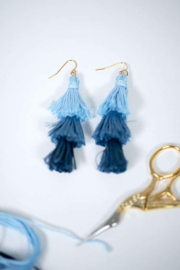Ombre stacked tassel earrings in three shades of blue floss on gold ear wires beside gold scissors and loose thread