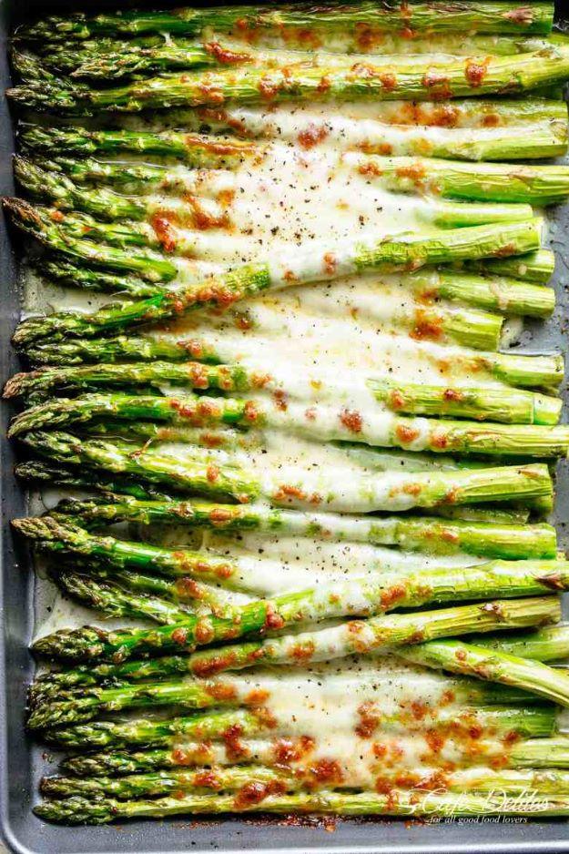 Cheesy garlic roasted asparagus on a sheet pan with green spears under melted browned mozzarella cheese