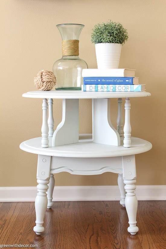 White two tier side table with turned legs holding a glass jar, books and a small plant on a wood floor