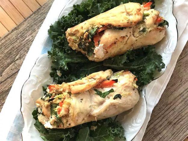 Quinoa stuffed chicken roll-ups on a platter over kale, two rolled chicken breasts with red pepper filling