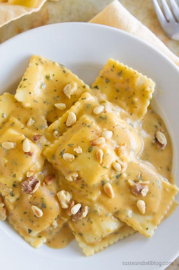 Ravioli in pumpkin alfredo sauce on a white plate, cheese ravioli coated in orange sauce with chopped nuts