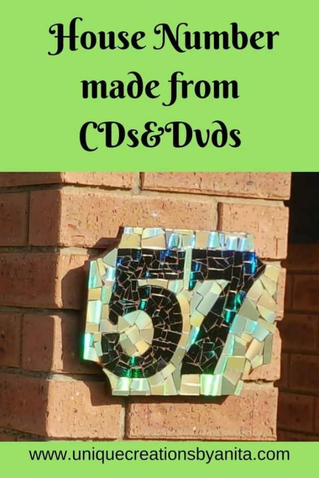 Typeset graphic reading House Number made from CDs and DVDs over a mosaic number plaque on a brick wall
