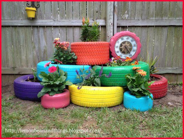Nine old tires painted purple, turquoise, orange and yellow stacked into a tiered flower bed against a wooden fence