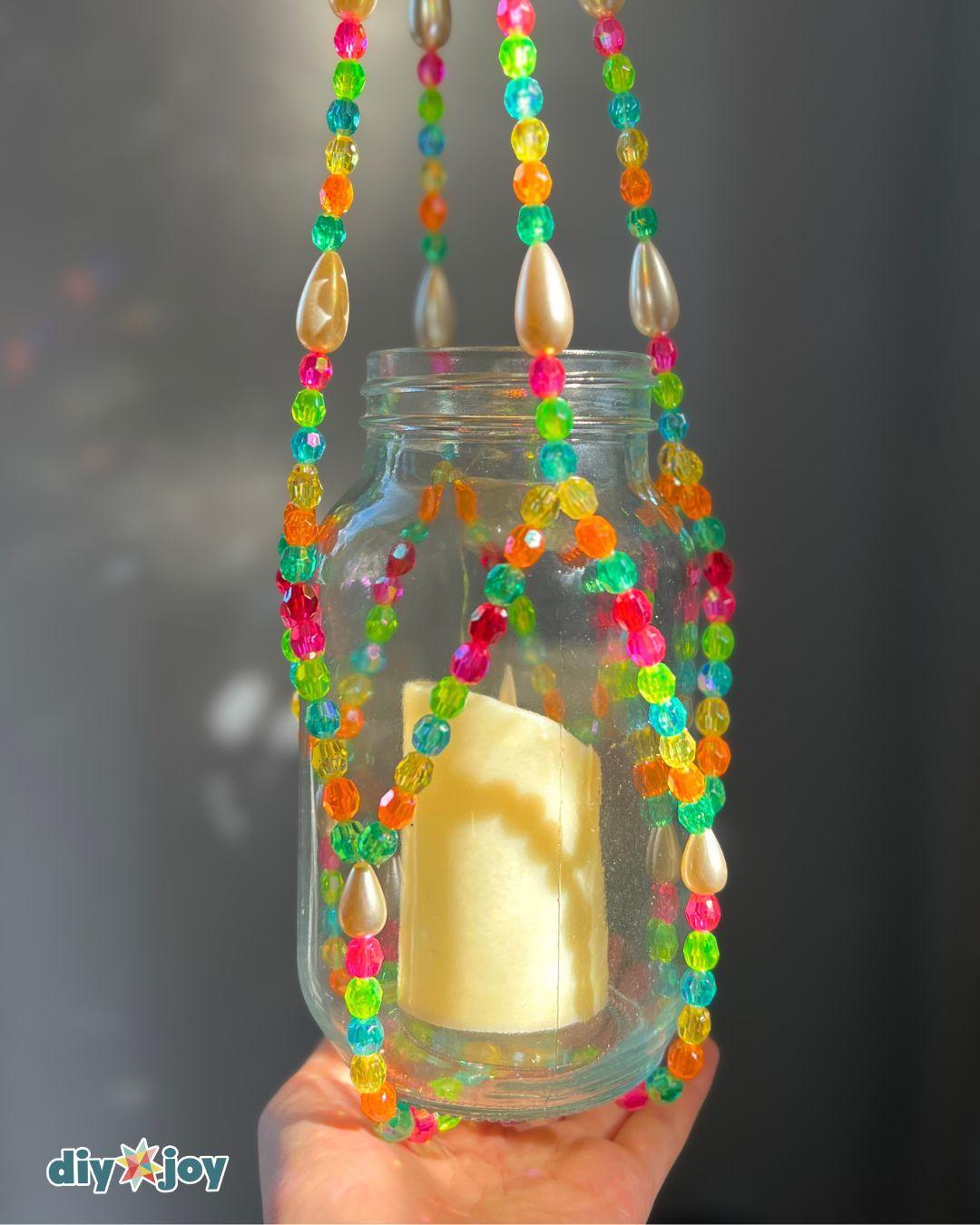 Homemade lantern hanging outdoors at dusk, a candle jar cradled in glass beads strung on clear fishing line