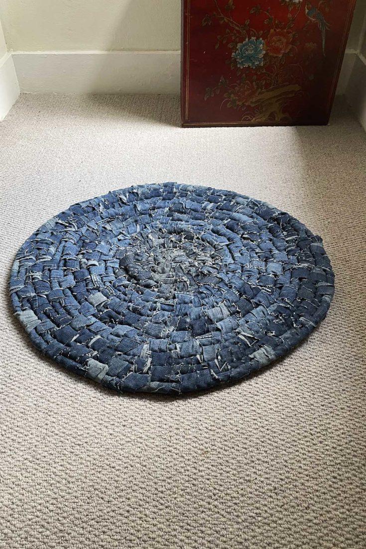 Round denim rag rug, a circular rug woven in spiralling coils from strips of blue denim, lying on pale carpet