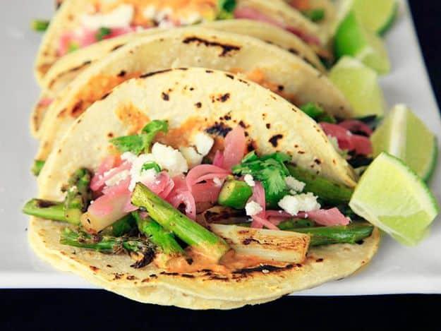 Charred asparagus tacos on a white platter, corn tortillas with asparagus, pickled onion, cheese and lime