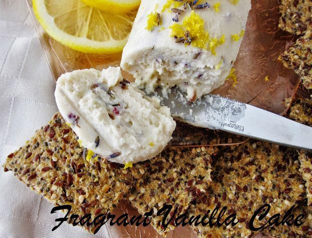 Raw lavender lemon chevre, a pale speckled nut cheese log being spread onto a dark seeded raw cracker