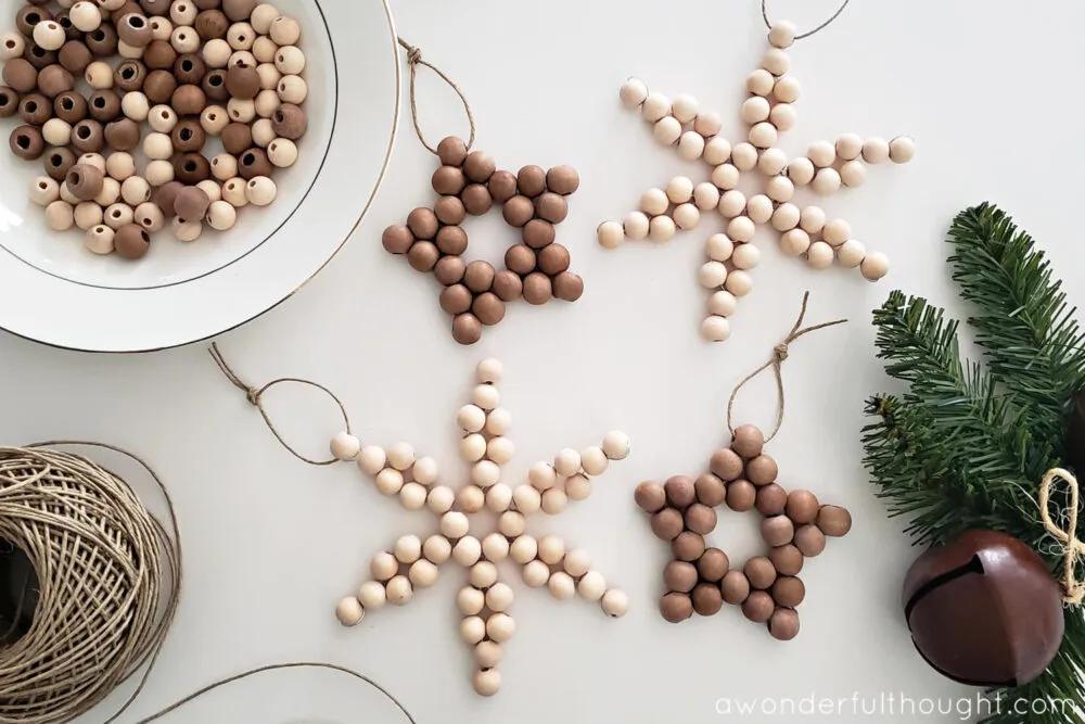 Four wood bead ornaments shaped as stars and snowflakes in natural and stained wood, tied with twine loops