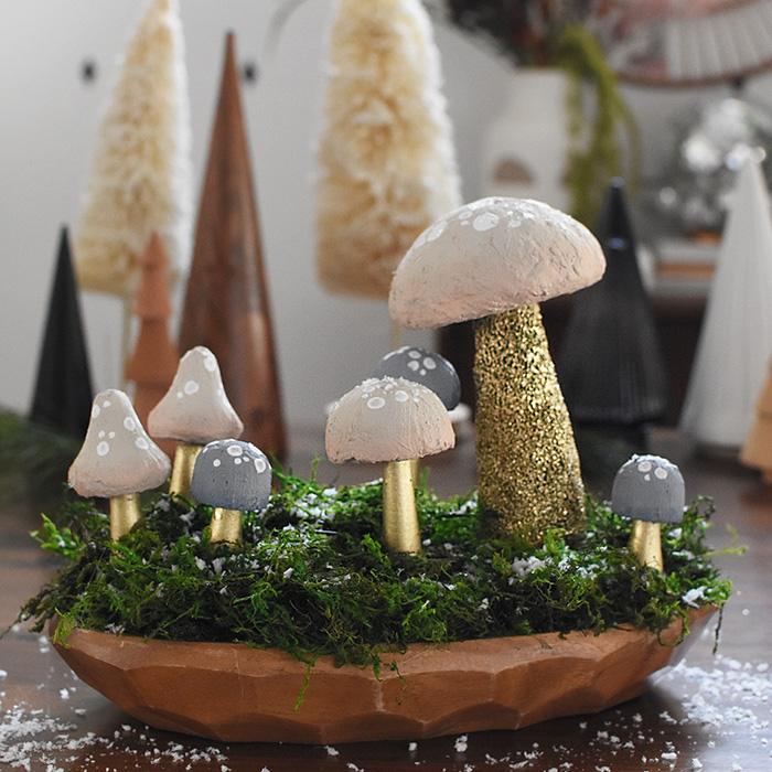 A cluster of painted DIY mushrooms in red, cream and rust on small wood stands arranged as a woodland Christmas centerpiece