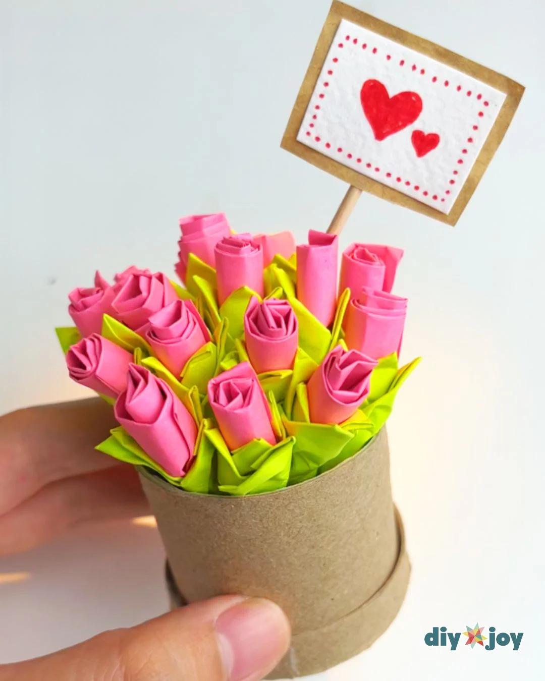 Finished paper flowers made from pink Post-it notes, with green leaves, standing in a cardboard tube vase