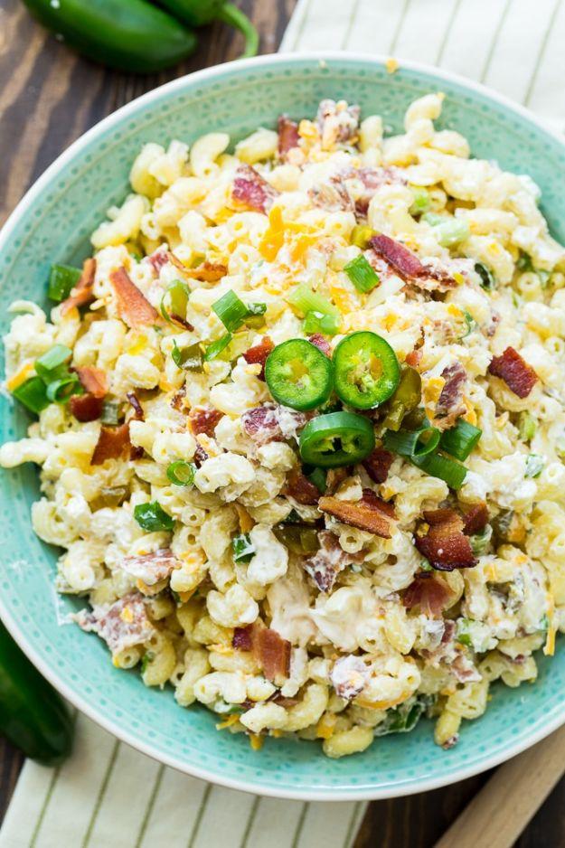Jalapeno popper pasta salad with bacon and shredded cheese, topped with fresh jalapeno slices in a green bowl
