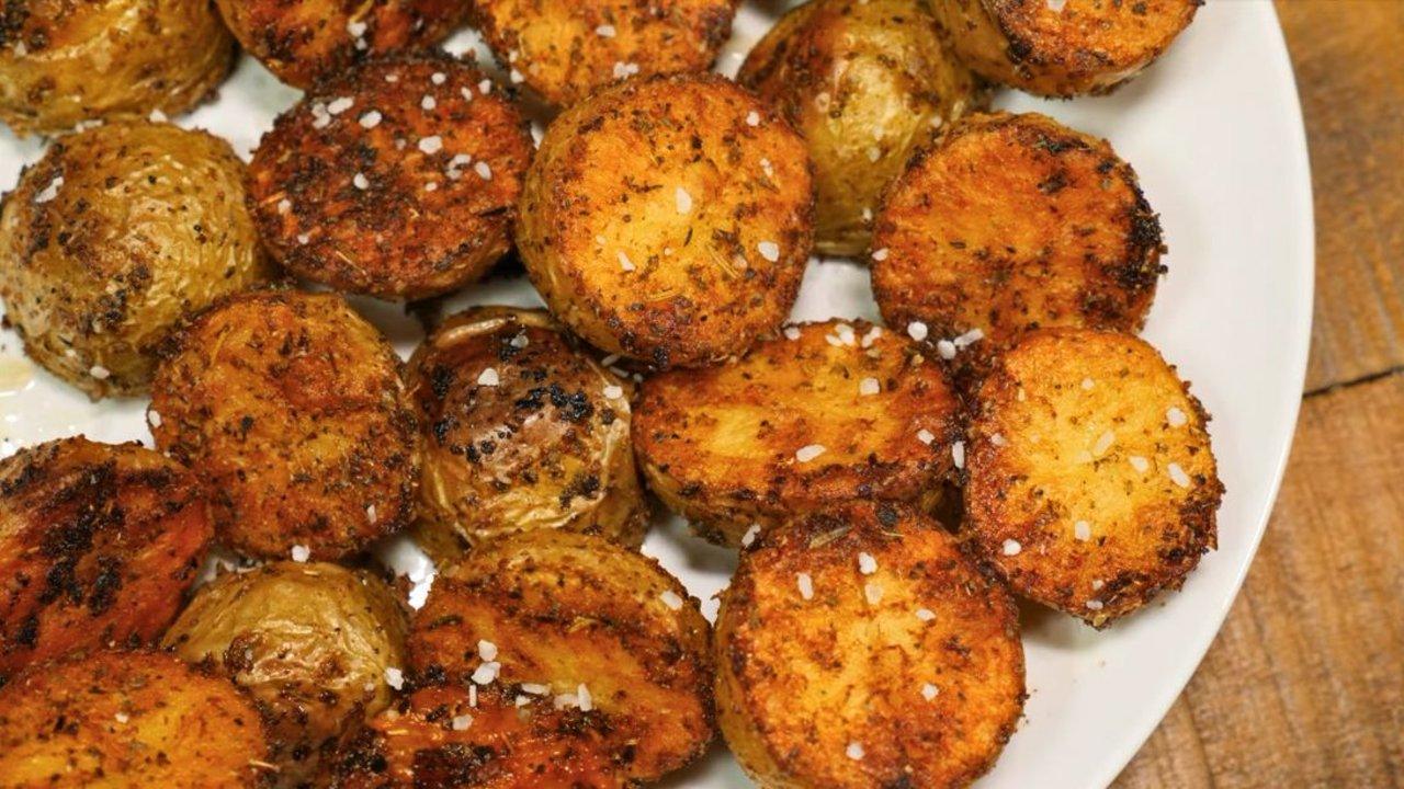 Crispy oven roasted baby potatoes, halved and golden brown on a foil lined baking sheet with dried herbs