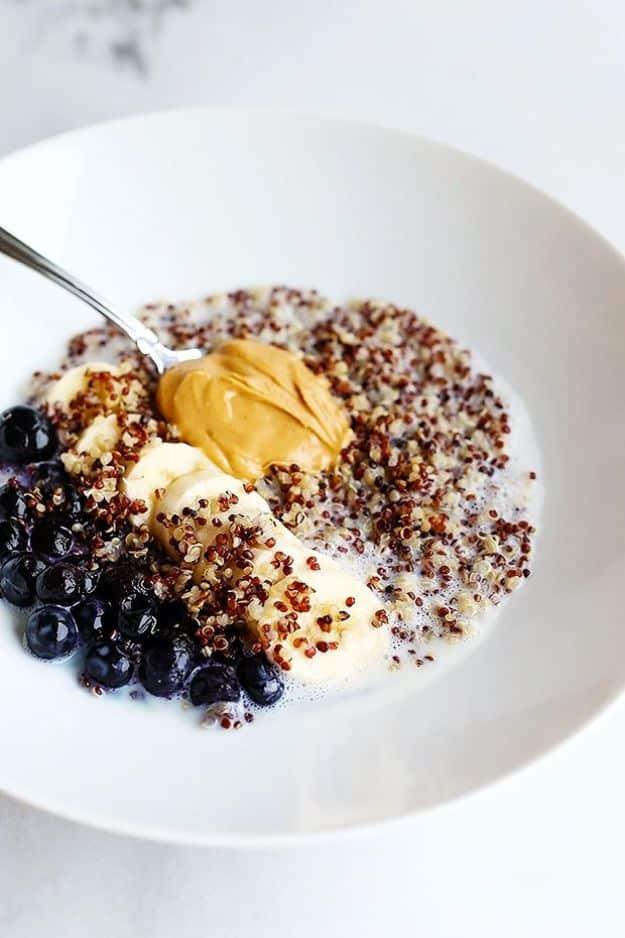 Five ingredient quinoa superfood breakfast bowl with sliced banana, blueberries and peanut butter in a white bowl