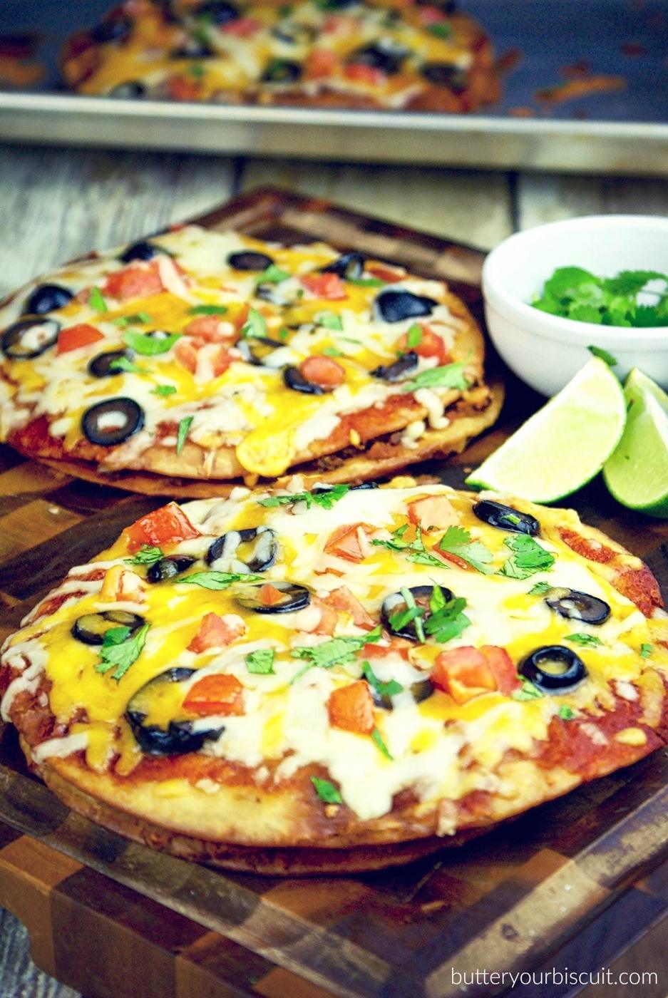 Two Mexican pizzas on fried tortillas with melted cheese, black olives, tomato and green onion with lime