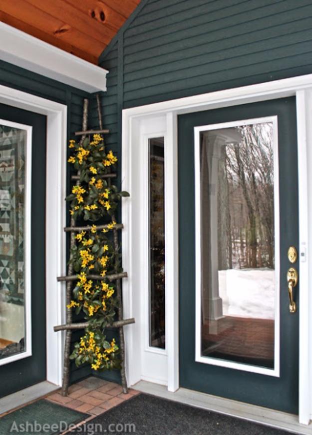 DIY curb appeal decorative twig ladder leaning beside a dark green front door with yellow forsythia woven through the rungs