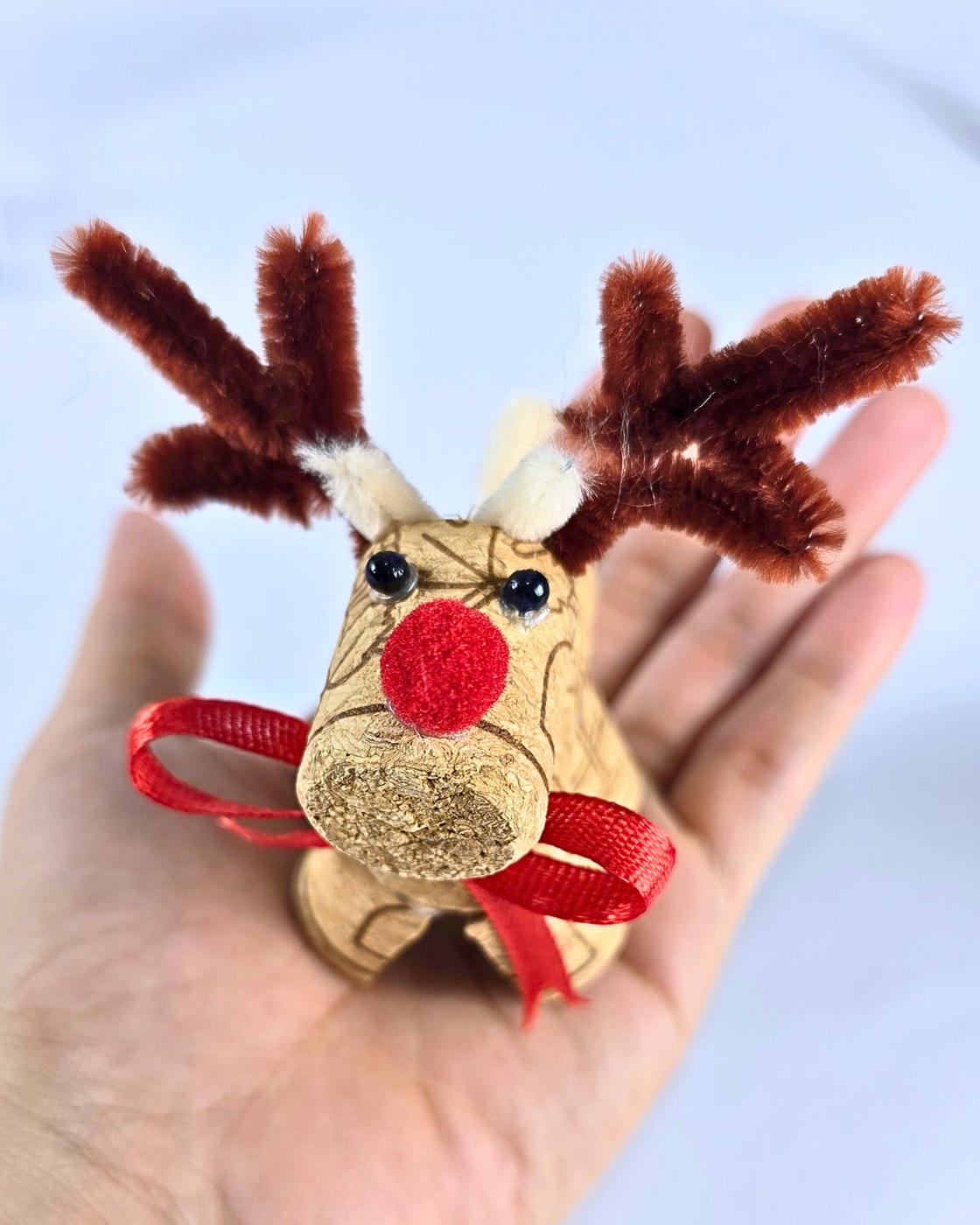 How to Make Reindeer - an open palm holding a cork reindeer with black bead eyes and a red nose