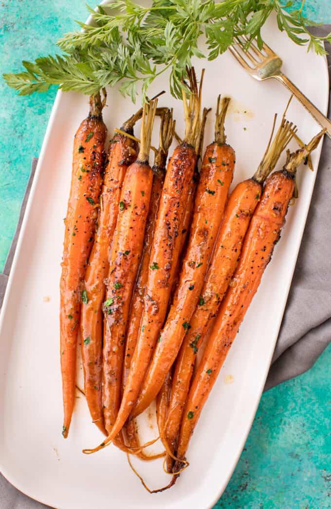 Glazed whole carrots arranged on a white rectangular platter over a turquoise surface in a finished side dish