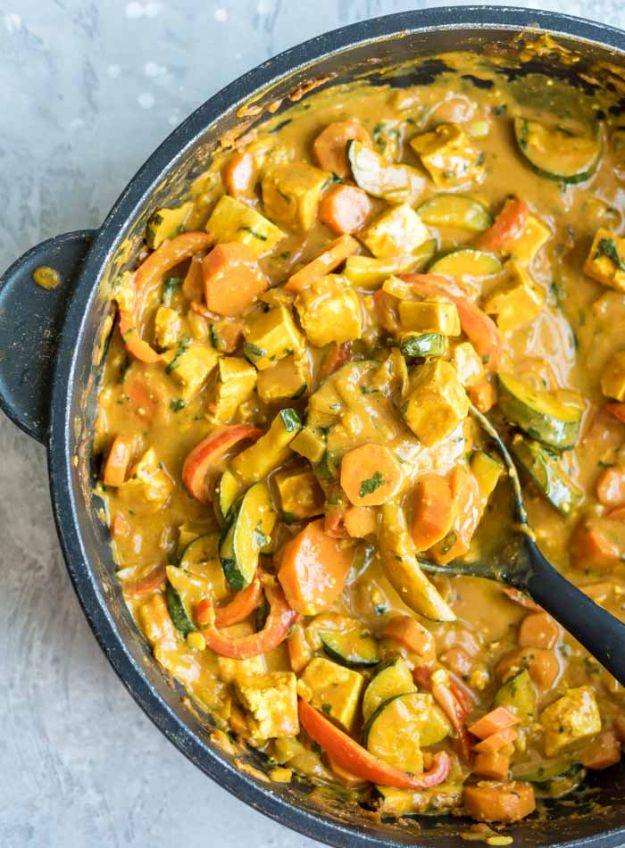 Vegan panang curry with tofu, carrots and zucchini in a dark skillet with a serving spoon on a pale surface