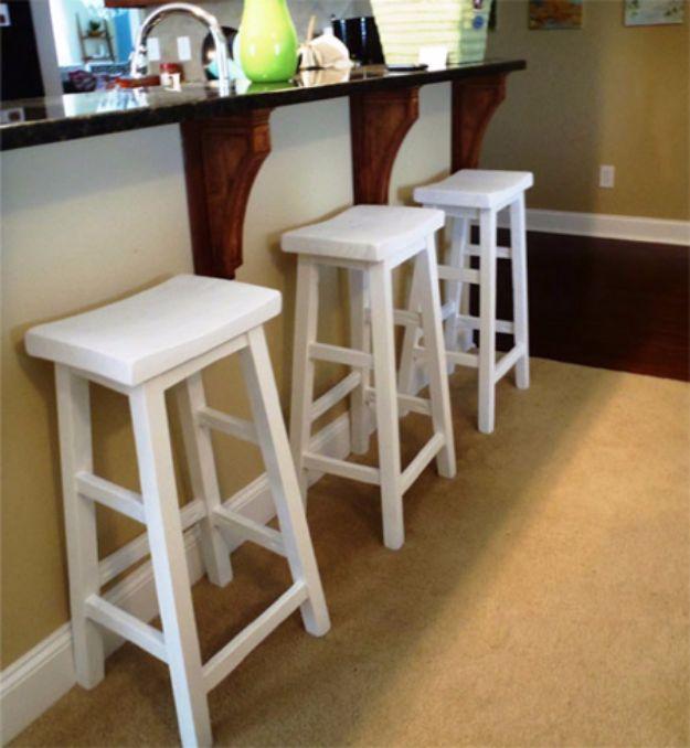Make your own bar stools, three white painted pine stools with shaped seats standing in a row at a dark kitchen counter