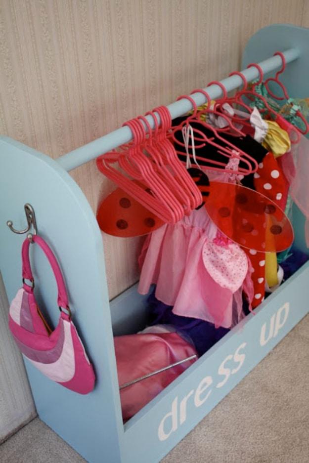 Dress up storage, a pale blue plywood costume stand with pink hangers of fairy wings and tutus and a bag on a side hook