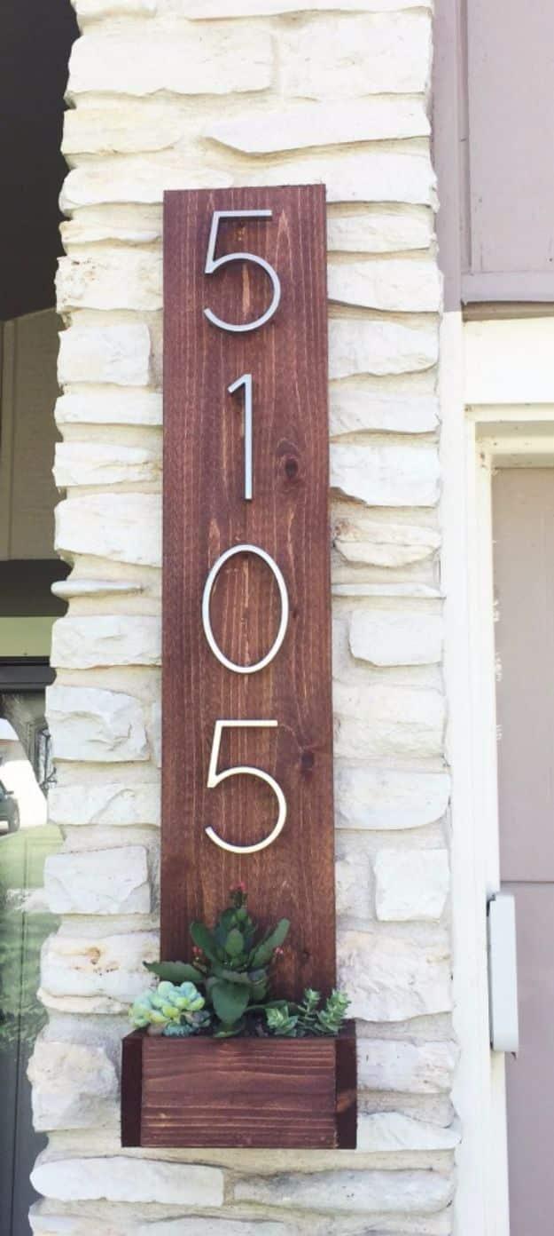 Vertical stained cedar board with large silver house numbers and a small succulent planter box mounted on a stone wall