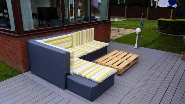 Dark blue upholstered pallet sectional with yellow and white striped cushions on a decking terrace by a house