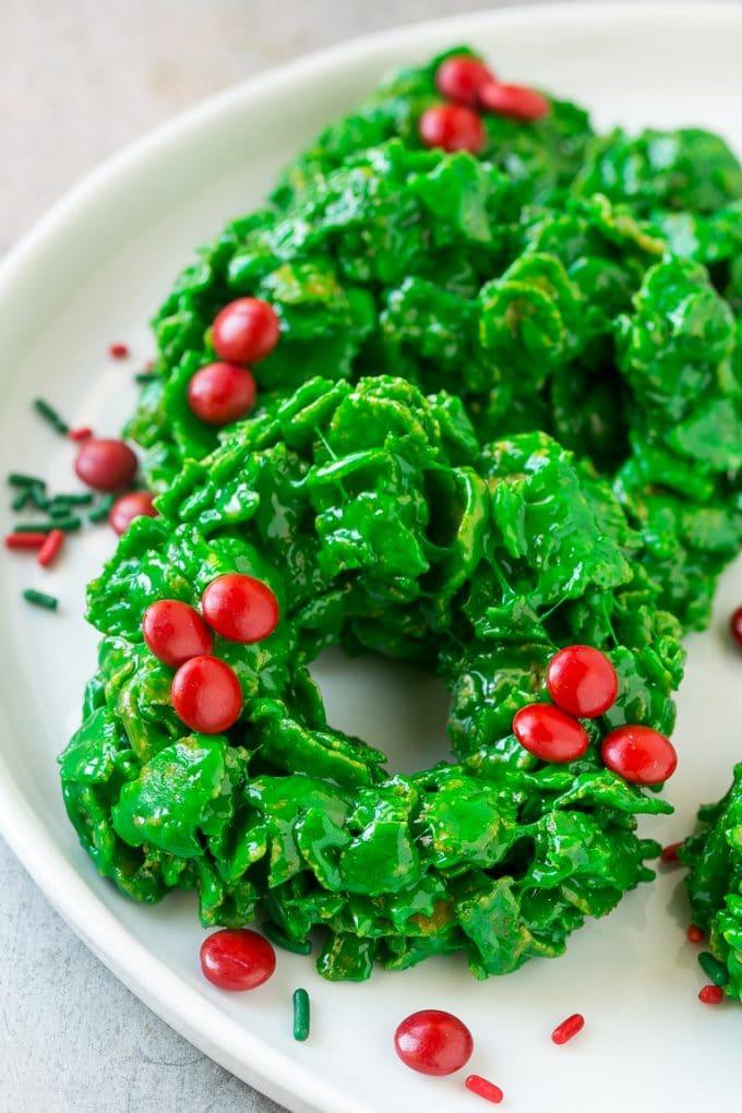 Bright green cornflake wreath cookies decorated with red candy coated chocolates and red and green sprinkles on a white plate