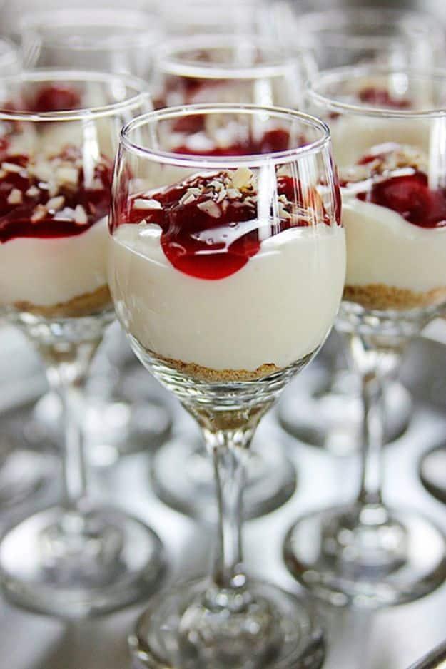 Row of small stemmed glasses filled with white cheesecake cream and dark red cherry topping on a grey surface