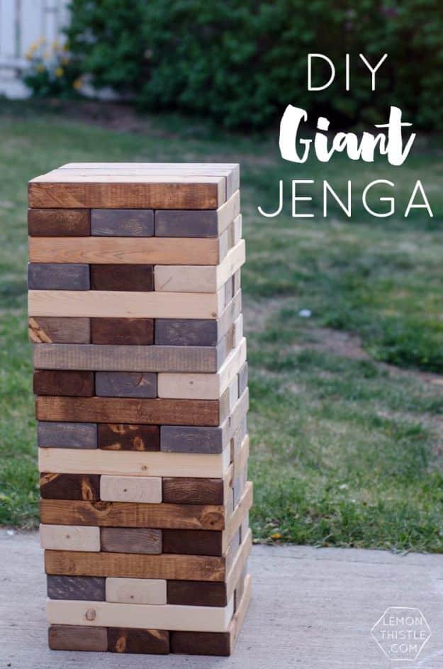 DIY giant Jenga tower stacked from stained 2x4 blocks in three wood tones, standing on a patio in a backyard
