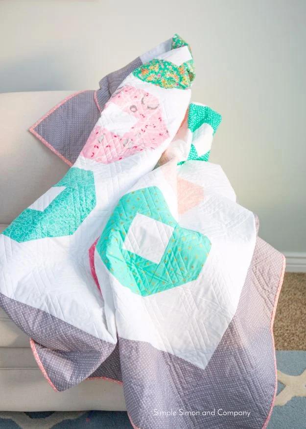 Shoo fly quilt in pink, aqua and mint blocks with white sashing and gray dot border, draped over a chair